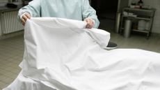 A photo showing a person wearing a blue clean suit lifting a white sheet on a surgical table.
