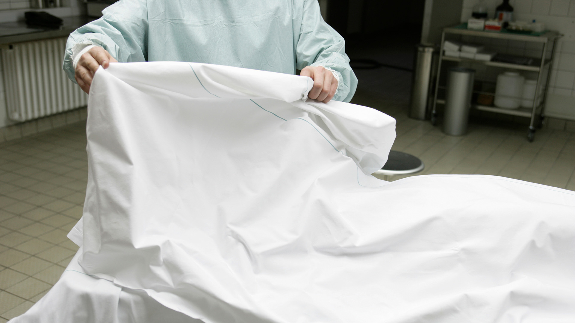 A photo showing a person wearing a blue clean suit lifting a white sheet on a surgical table.