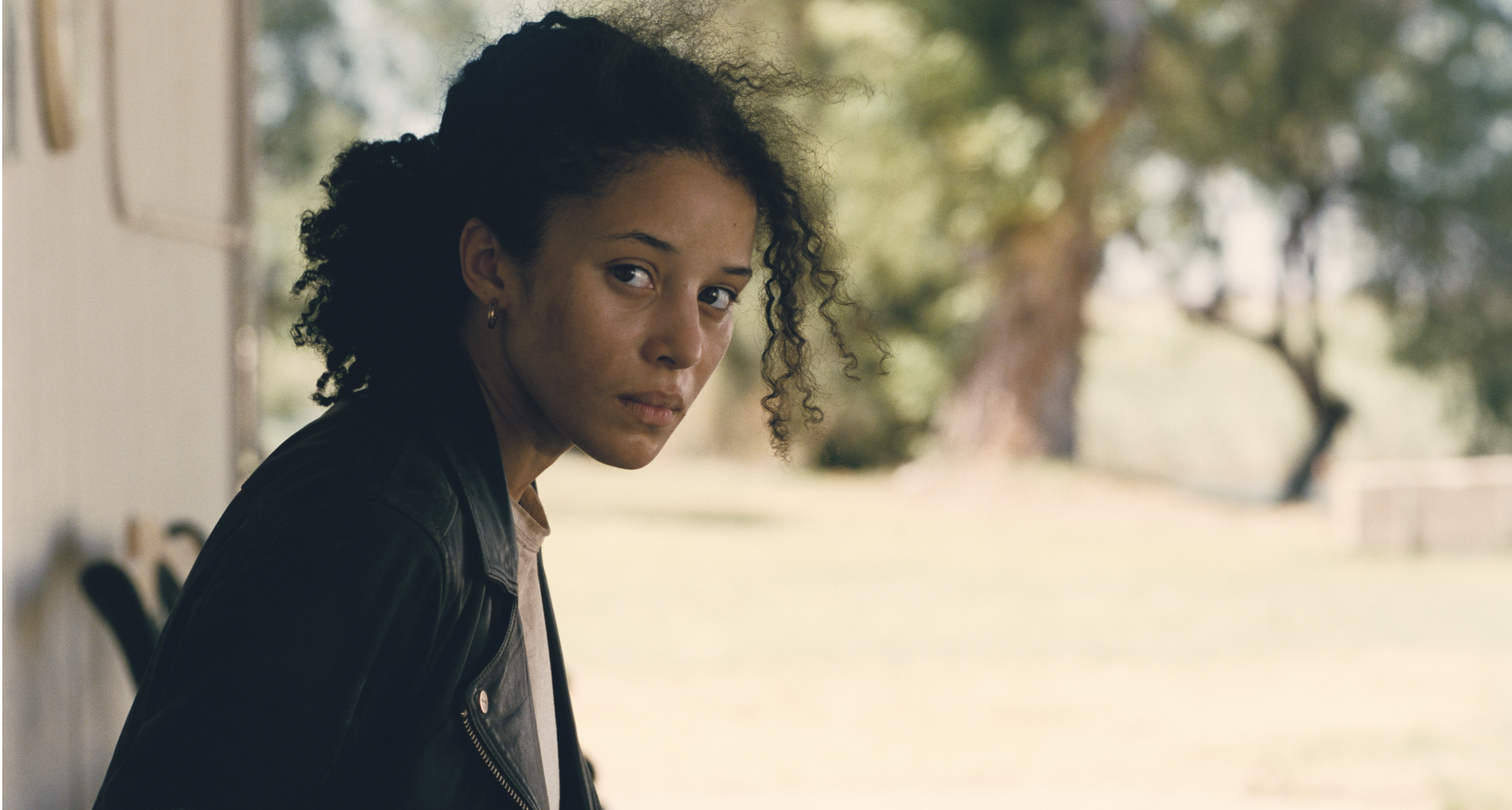 chase infiniti as willa looking to her right wearing a black leather jacket in one battle after another