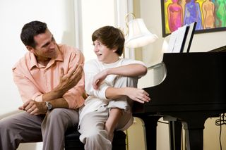 A dad and teen boy sit talking in a living room