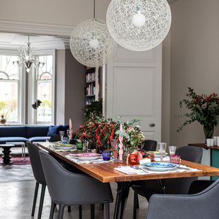 Dining room area with a wooden dining room table decorated with flowers and cutlery, with white modern lights hanging above the table