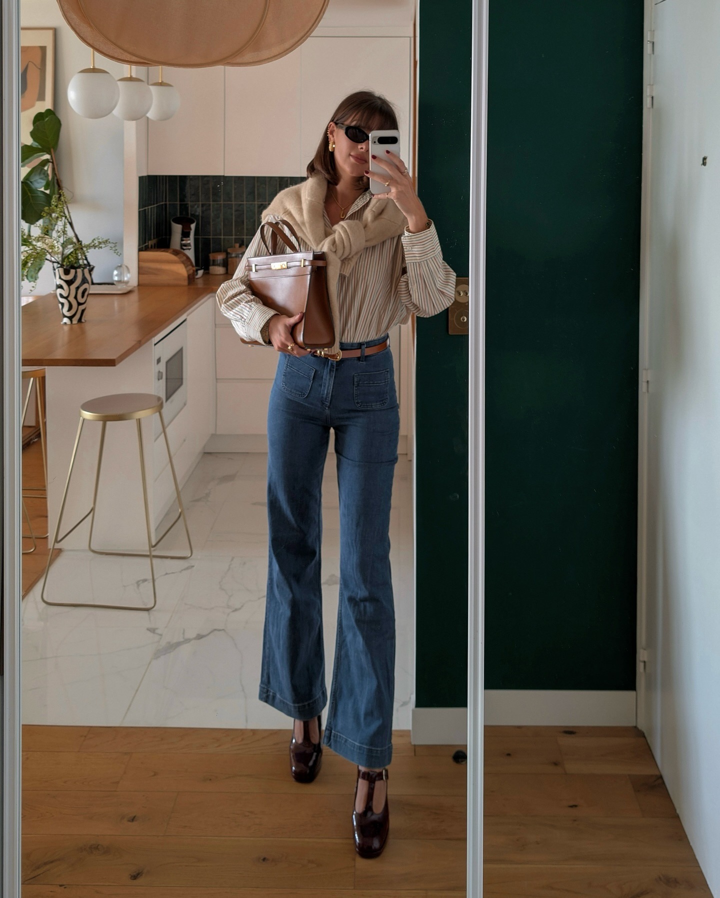 Influencer @juliesfi wears cropped flared jeans with heeled t-bar shoes and a button-down tucked into her jeans. She styles a knit over her shoulders.