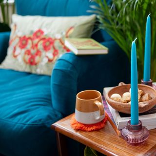 blue velvet armchair with cushion, side table and candles with mug and houseplant