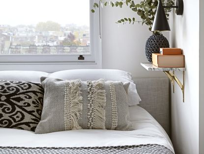A bed in front of a window decorated with a fringed, boho style pillow