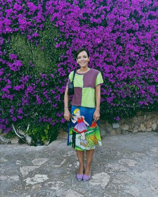 Lily Allen wears a printed skirt, a color-block T-shirt, purple flats, and a black handbag.