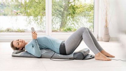 A woman lying on a Beurer MG 280 yoga and stretch mat, using one of the best massagers