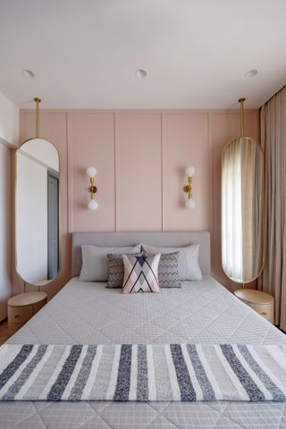 A bedroom with pink wall paint and two long mirrors on either side