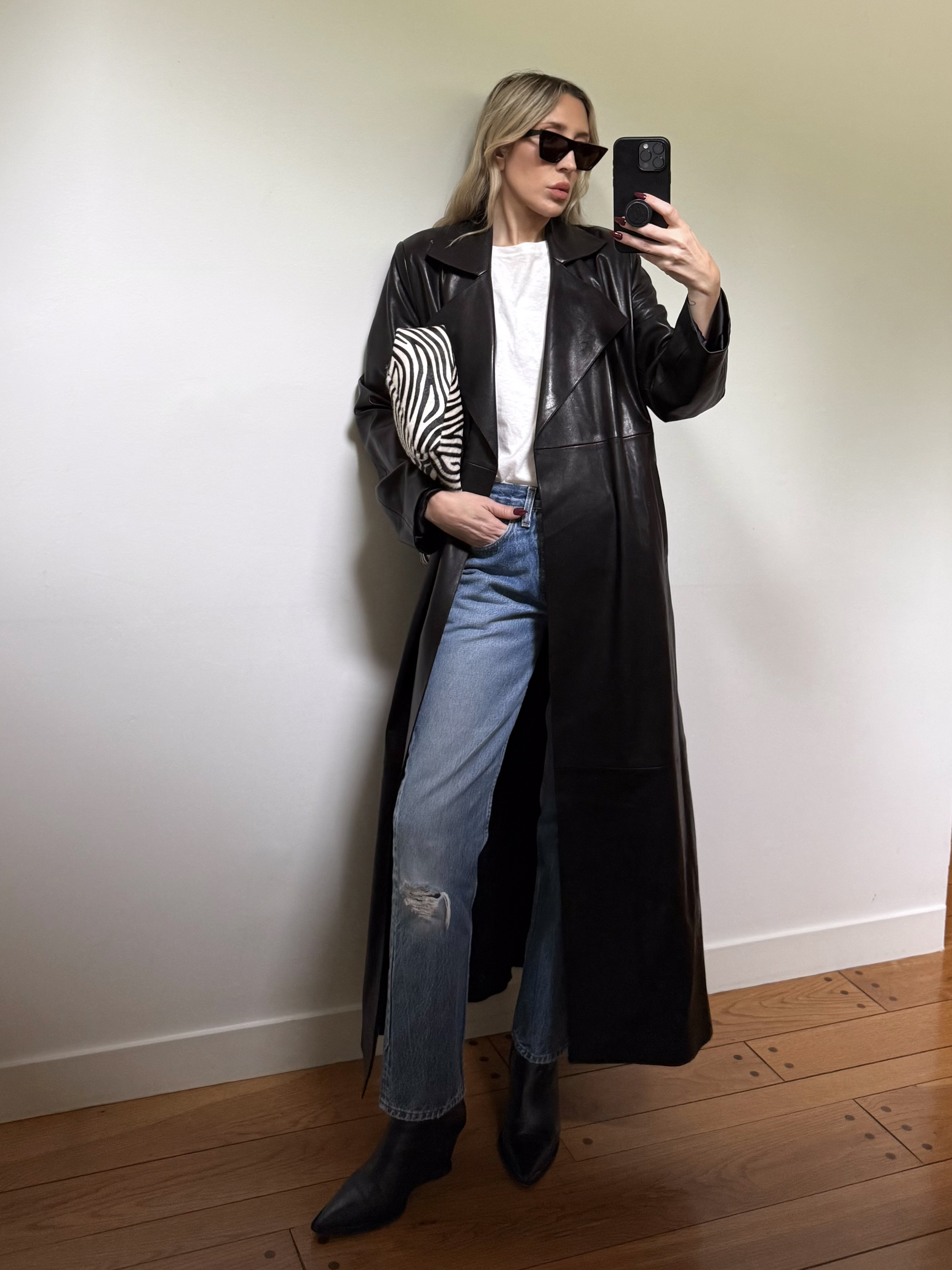 Angela Fink wearing a leather trench coat, a white tee, jeans, and boots