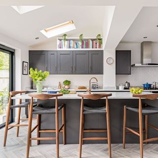 white modern kitchen with skylights, dark cabinetry, wooden bar stools