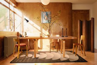 Dining space with curved walls panelled in wood, wooden dining table and chairs, wood floor, and undulating wooden screen