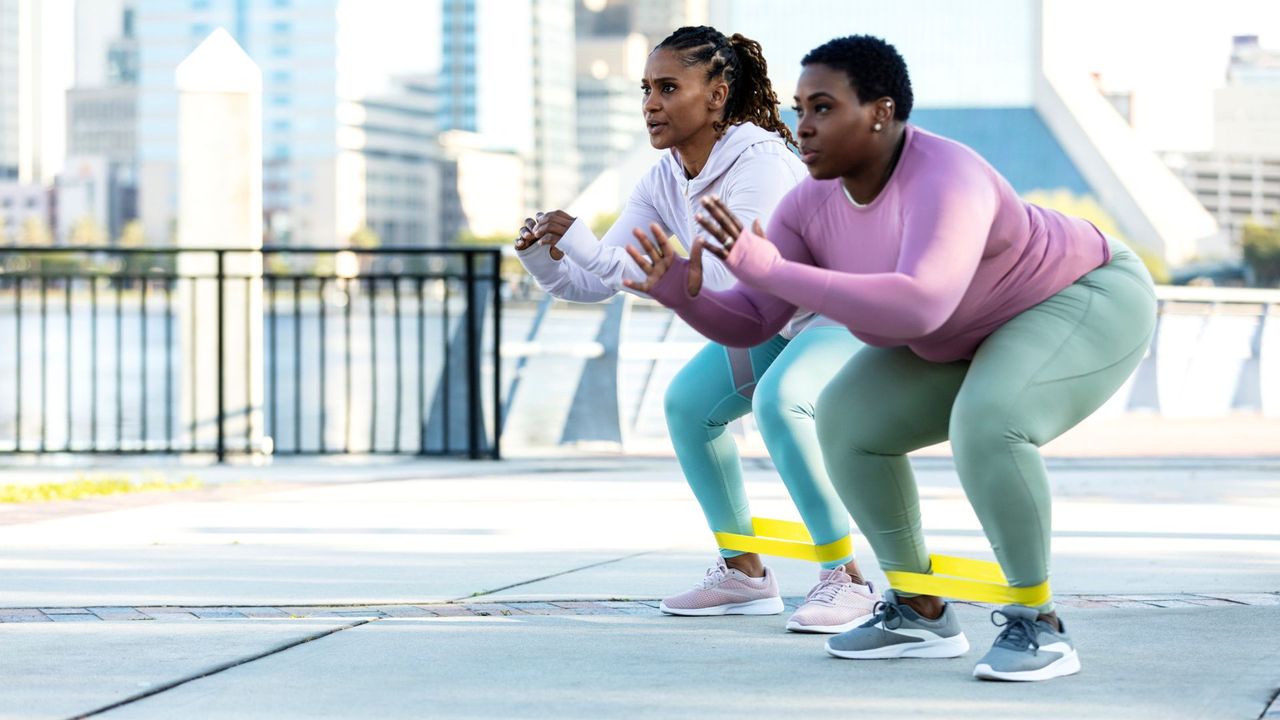 Two women taking part in a resistance band workout outdoors