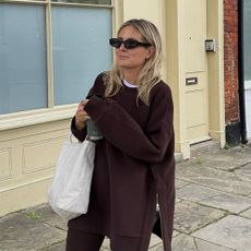 Influencer @lucywilliams02 stands outside in London wearing burgundy leggings with a burgundy jumper and black sunglasses.