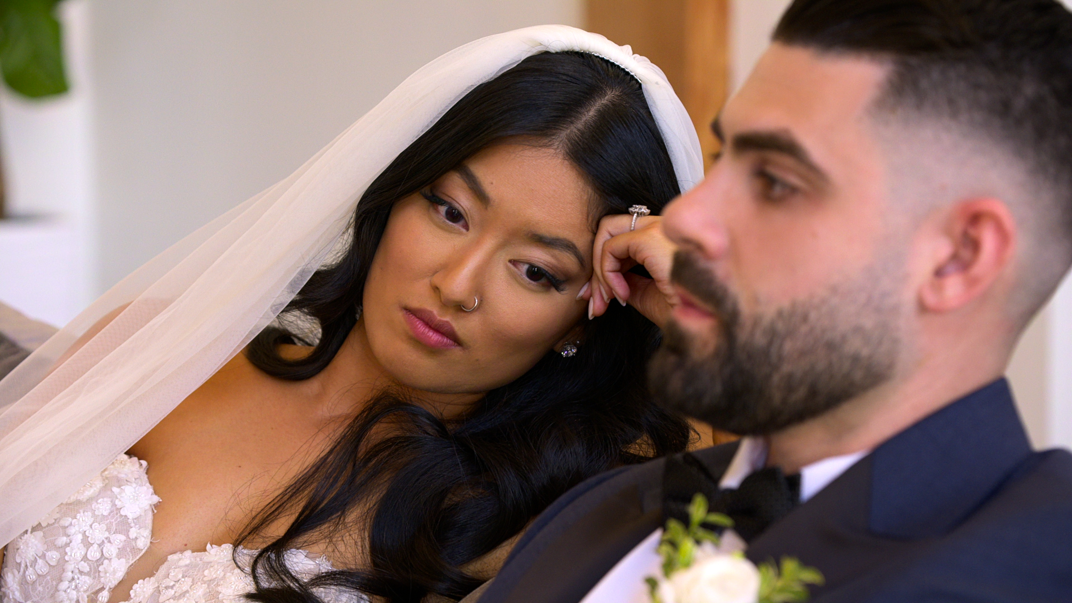 A woman in a wedding dress and veil (Emma Betsinger) frowns while resting her head on her hand, sitting next to a man in a tux (Mike Gibney) in the 'Love Is Blind' season 10 finale.