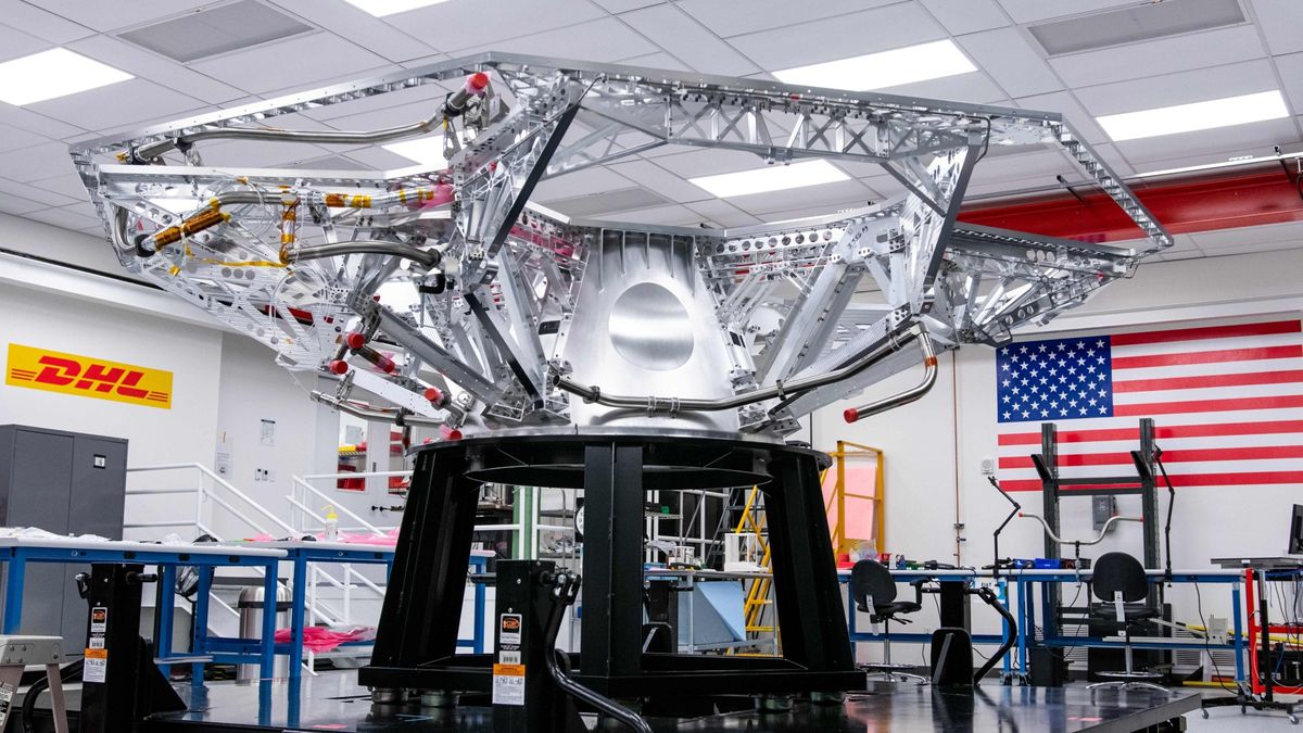 a metal skeleton of a cube-shaped spacecraft inside a laboratory cleanroom