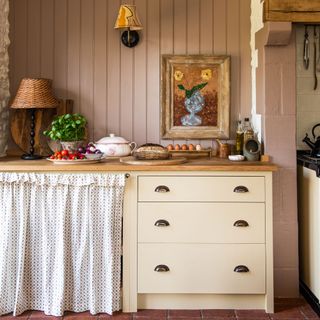 kitchen with pink panelled walls, cream cabinets and skirt