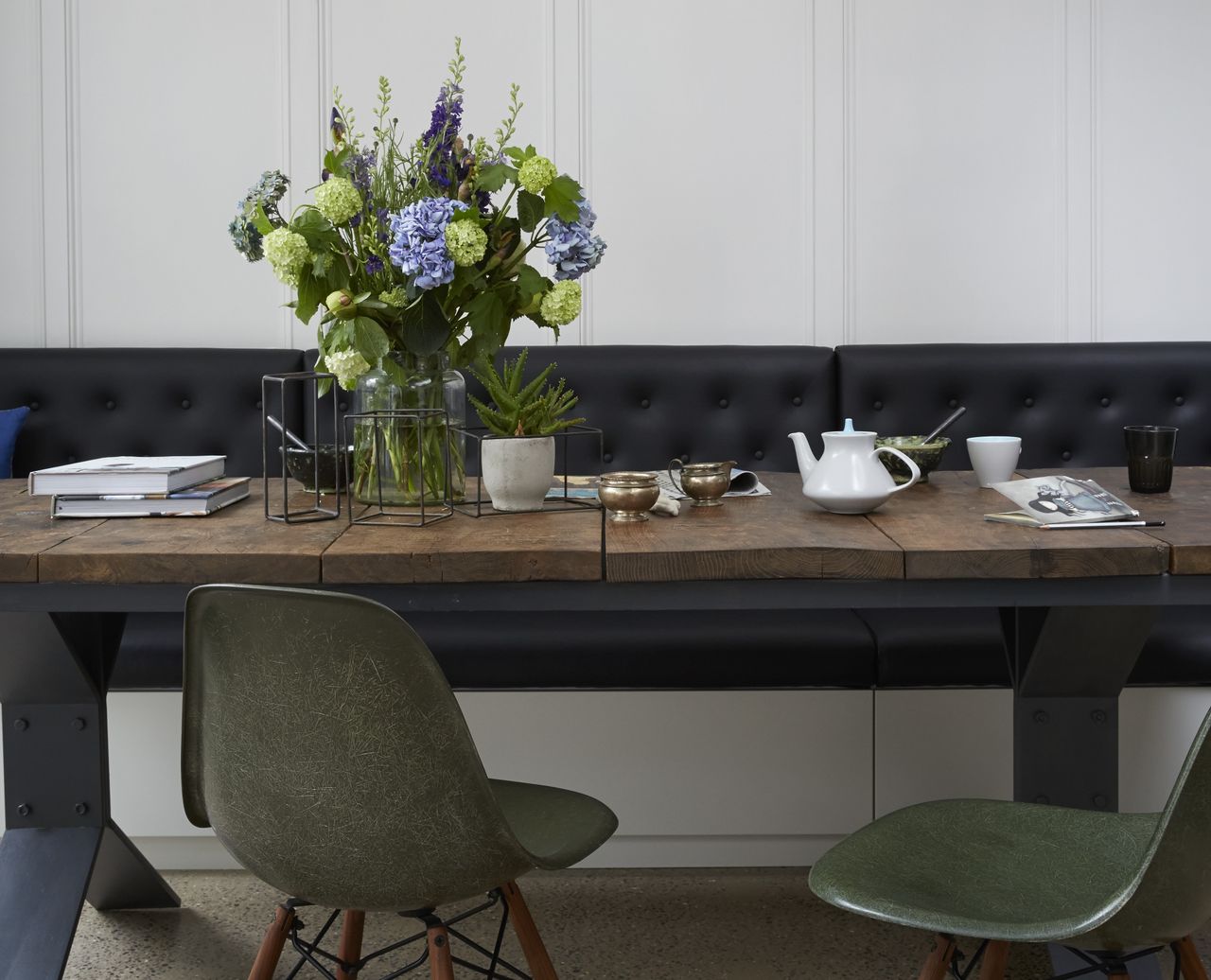 A vase of flowers on a wooden dining table with blue, green and purple flowers