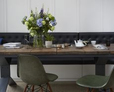 A vase of flowers on a wooden dining table with blue, green and purple flowers