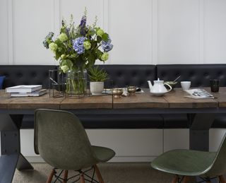 A vase of flowers on a wooden dining table with blue, green and purple flowers