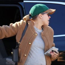 Sofia Richie wearing a camel jacket, gray T-shirt, burgundy pants, a baseball cap, and Uggs