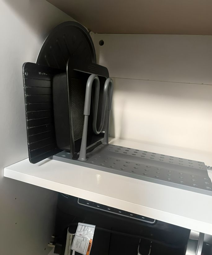 A grey peggy organizer being used in a white cabinet to organize pots and pans