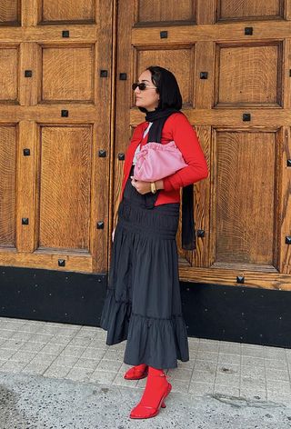 a photo showing what colors go with red, specifically a woman wearing a red cardigan with a white t-shirt, pink bag, black skirt, red tights and red sandals