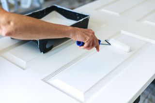 A man painting a door white with a small roller.