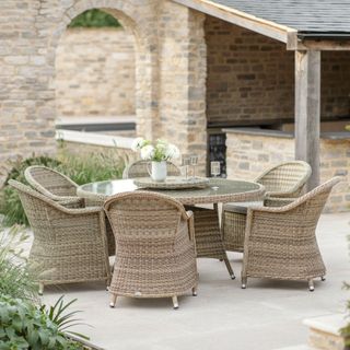 A rattan dining table and chair on a paved patio