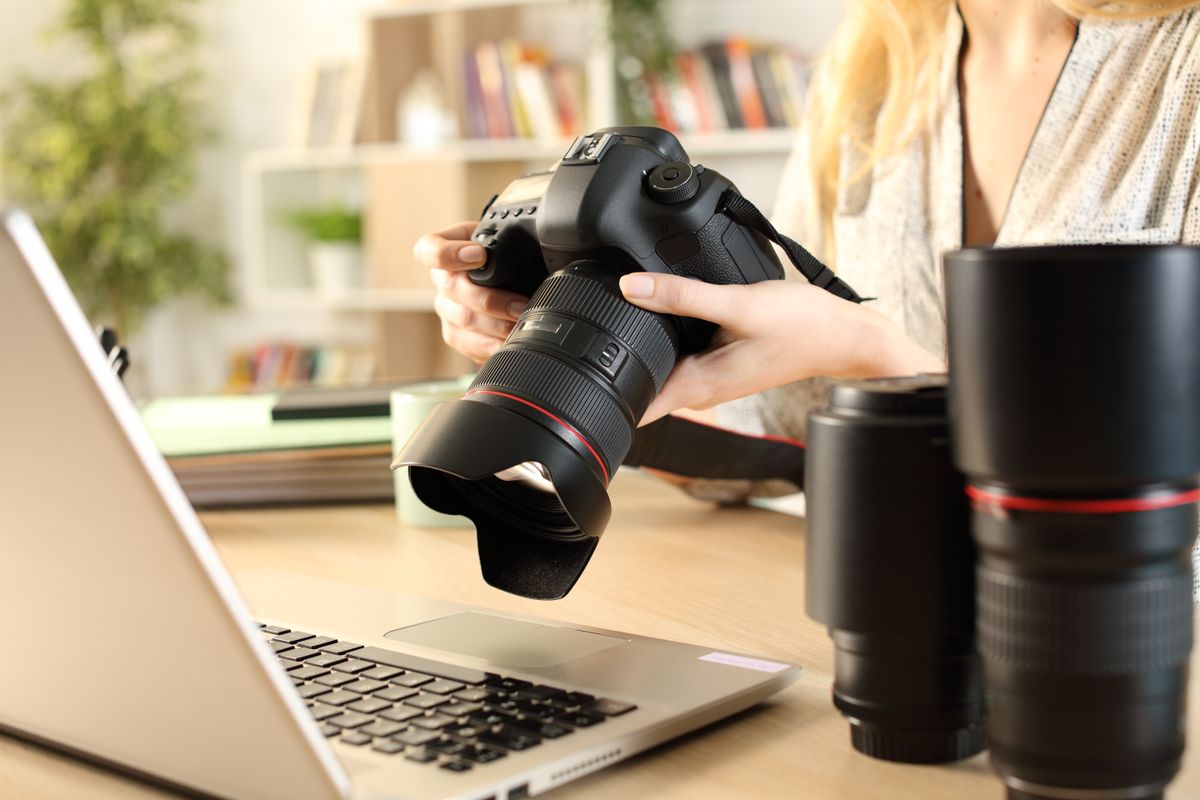 Pro photographer&#039;s hands checking camera at a desk with laptop and spare lenses- stock photo