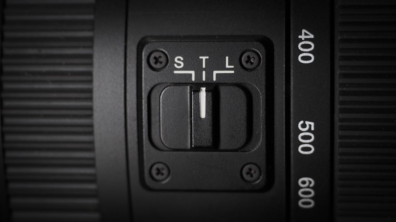 OM System M.Zuiko 150-600mm f/5.0-6.3 IS lens, mounted to an OM System OM-1 Mark II, on a wooden surface lit with moody lighting