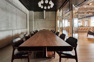 Long, wooden conference table and chairs, beside exposed concrete walls