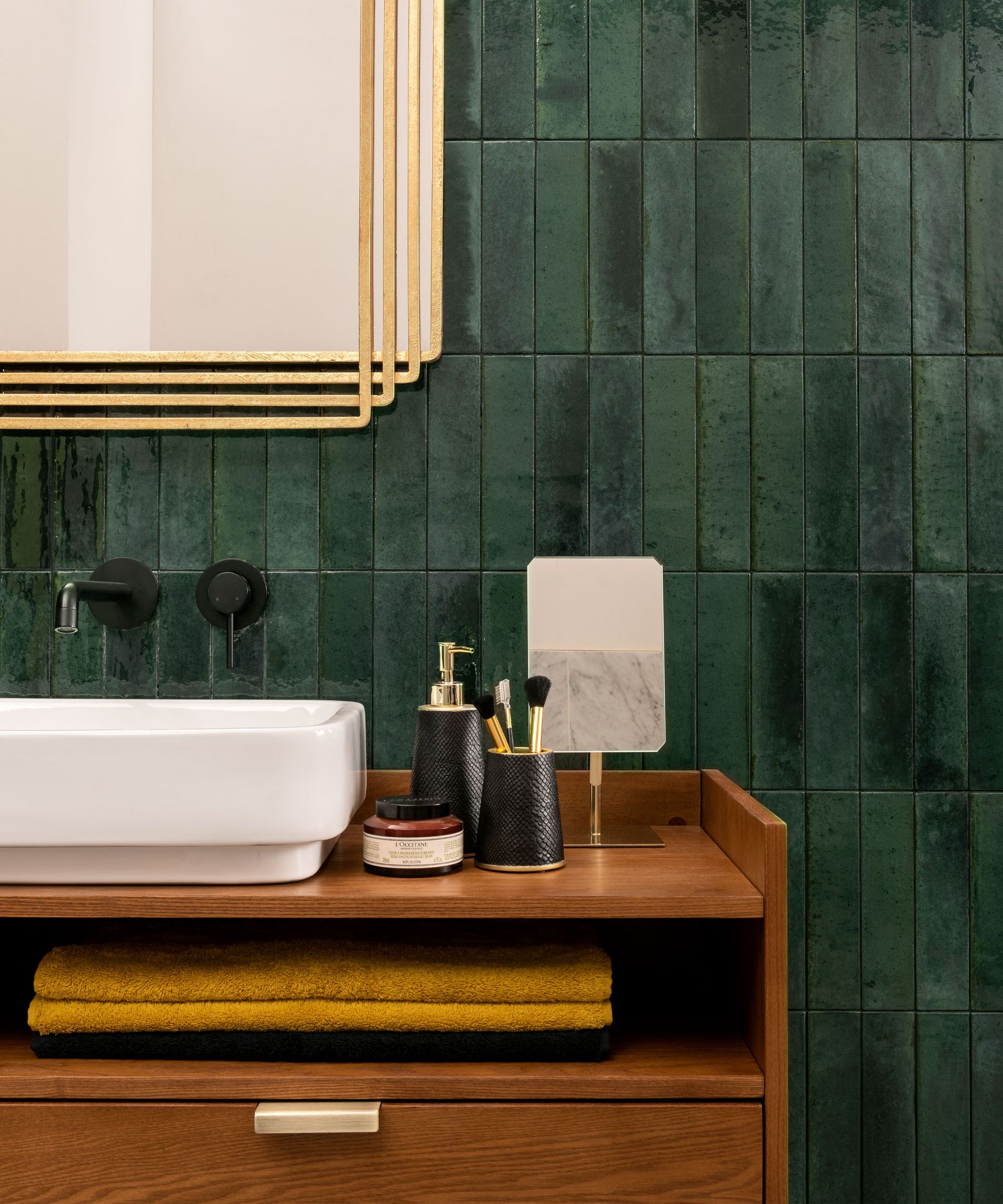 Close up of bathroom vanity, green vertical tiles, brass art deco mirror, wooden sink, yellow towel