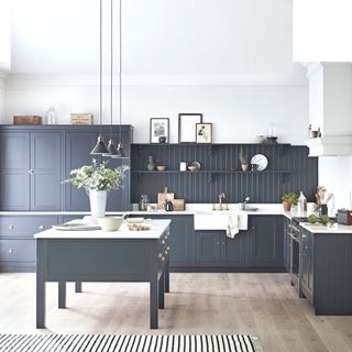 dark blue kitchen cabinets and matching dark wall panelling set against white walls and ceiling and light wood flooring
