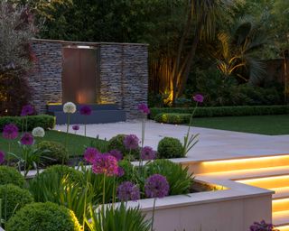 sleek water feature, pale paving and lit steps in a luxury garden desiign