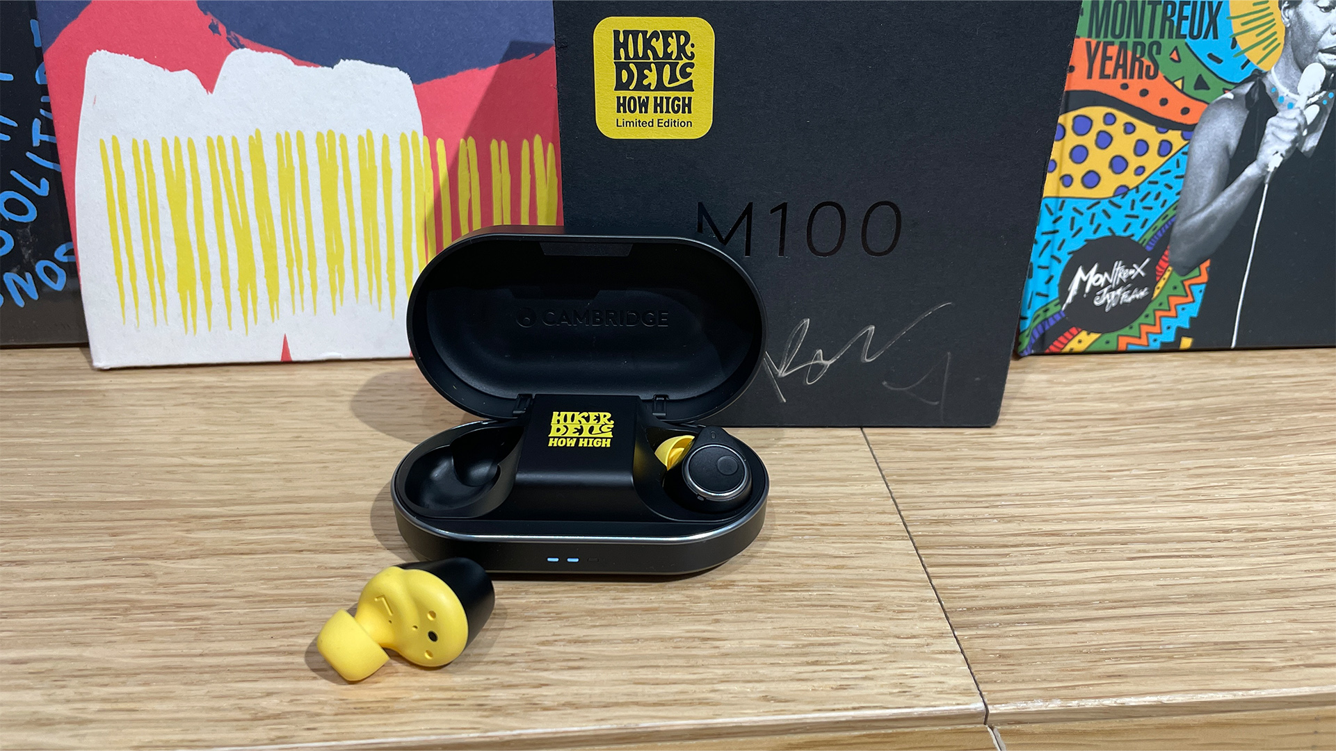 Cambridge Audio Melomania M100 wireless earbuds on wooden top with one bud out of case