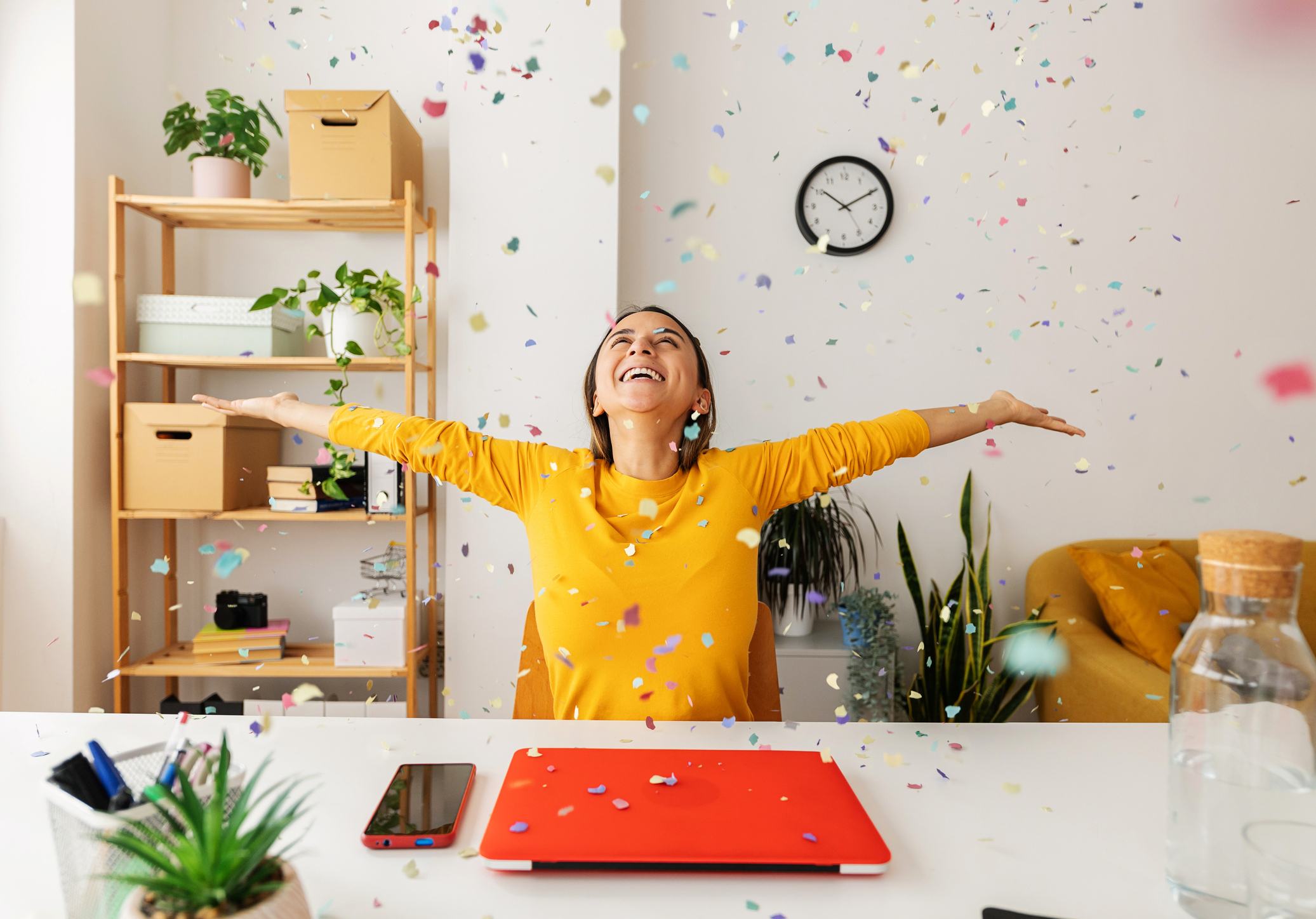 Woman sitting at desk, celebrating and being showered in confetti