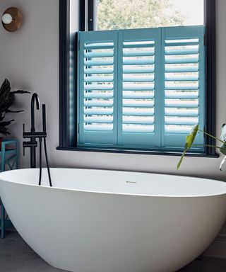 White bathtub in small bathroom with blue shutters and black window frame