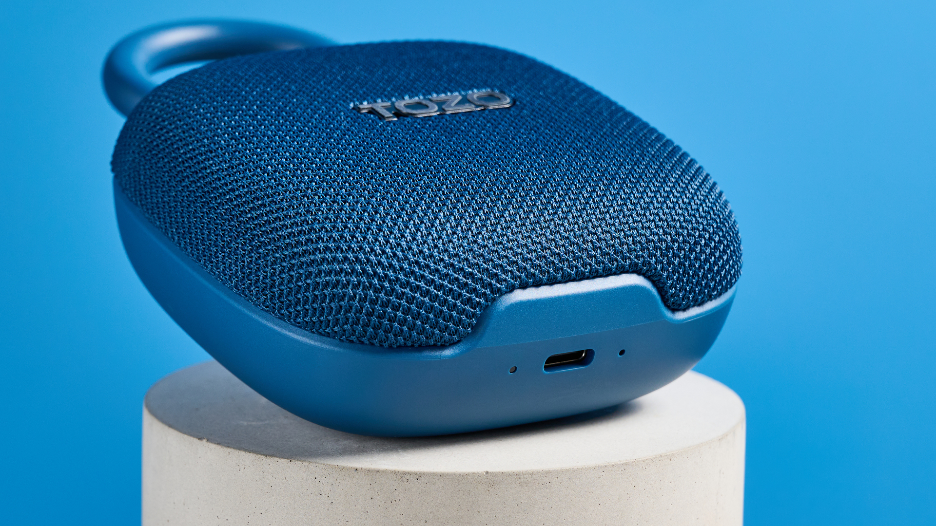 Tozo PE1 speaker in blue with built-in clip photographed on a blue background.