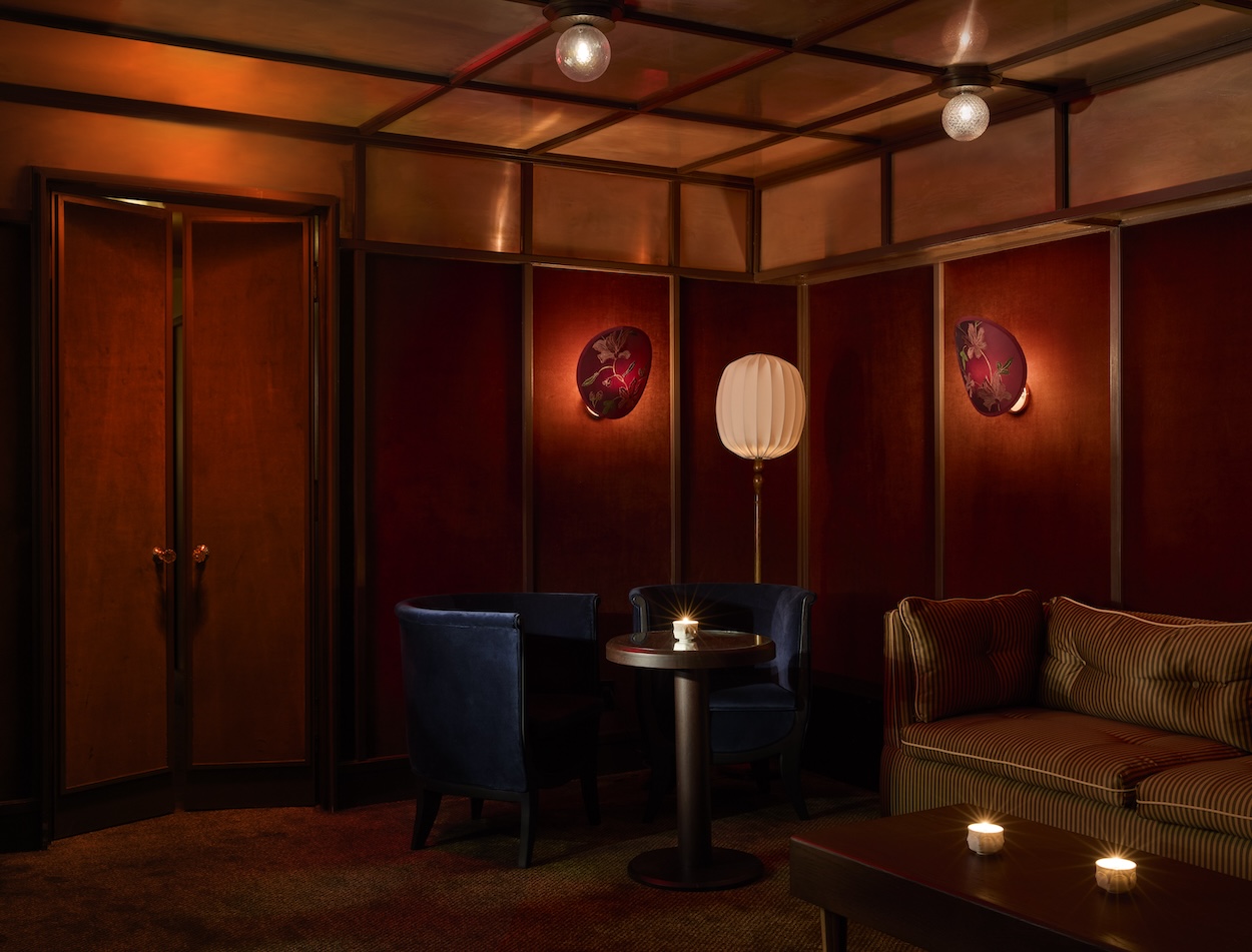 A sumptuously decorated bar features warm Art Deco lighting, refined cabinetry, and curtain-paneled walls.