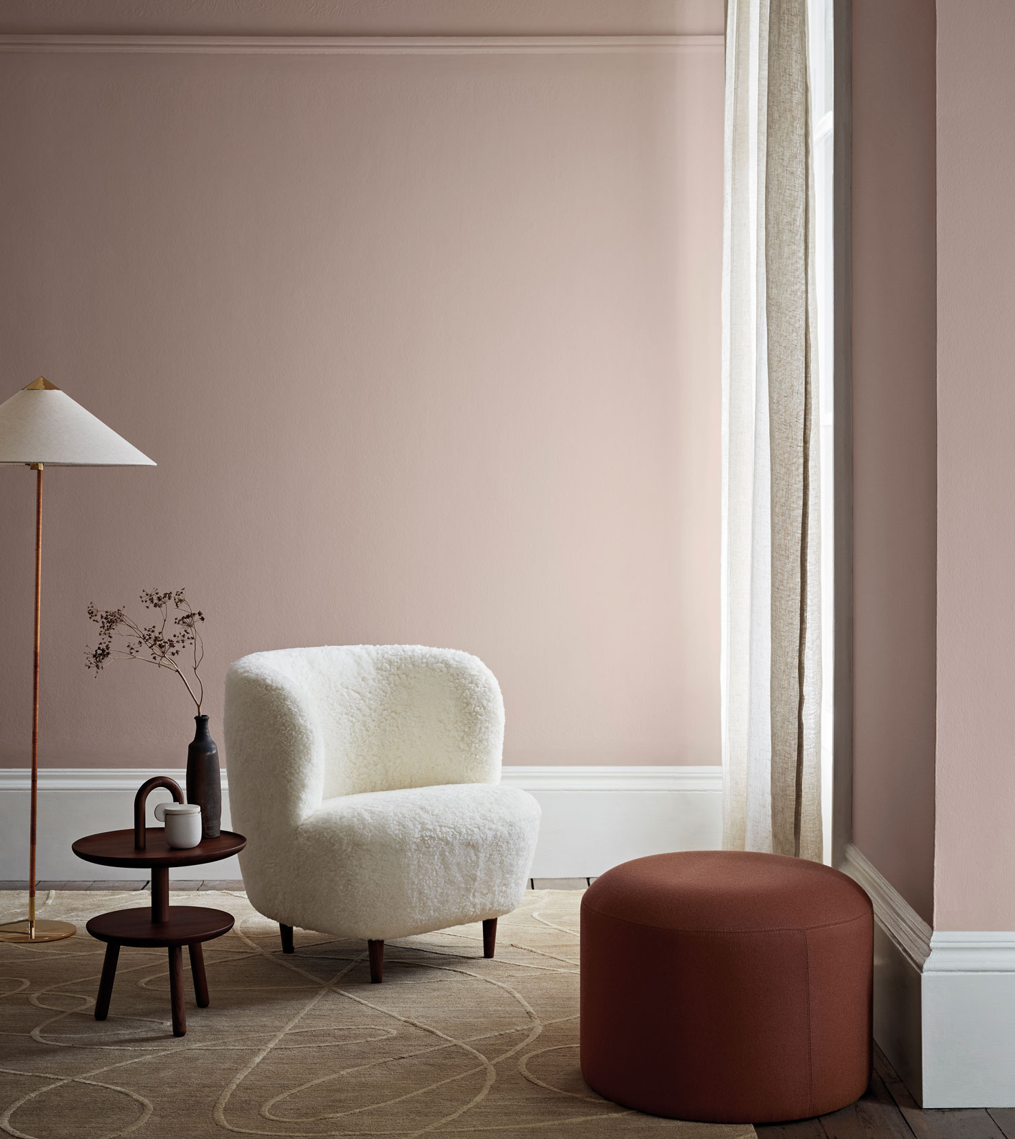 A pastel living room color scheme with pale blush pink walls, a white fur armchair and white drapes and skirting boards.