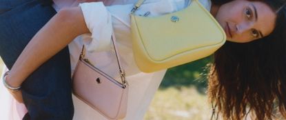Model standing at a right angle with two Kate Spade handbags one pastel pink and the other pastel yellow