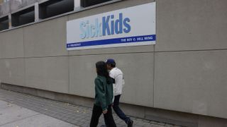 People walk by a SickKids sign by The Hospital for Sick Children in Toronto
