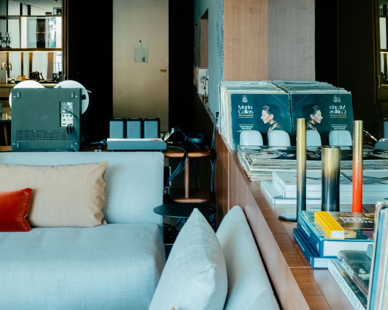 A high-fidelity listening suite fitted with retro-inspired music gear features floor-to-wall windows capturing the natural beauty of a lake and mid-century furniture with natural hues and textural furnishings.