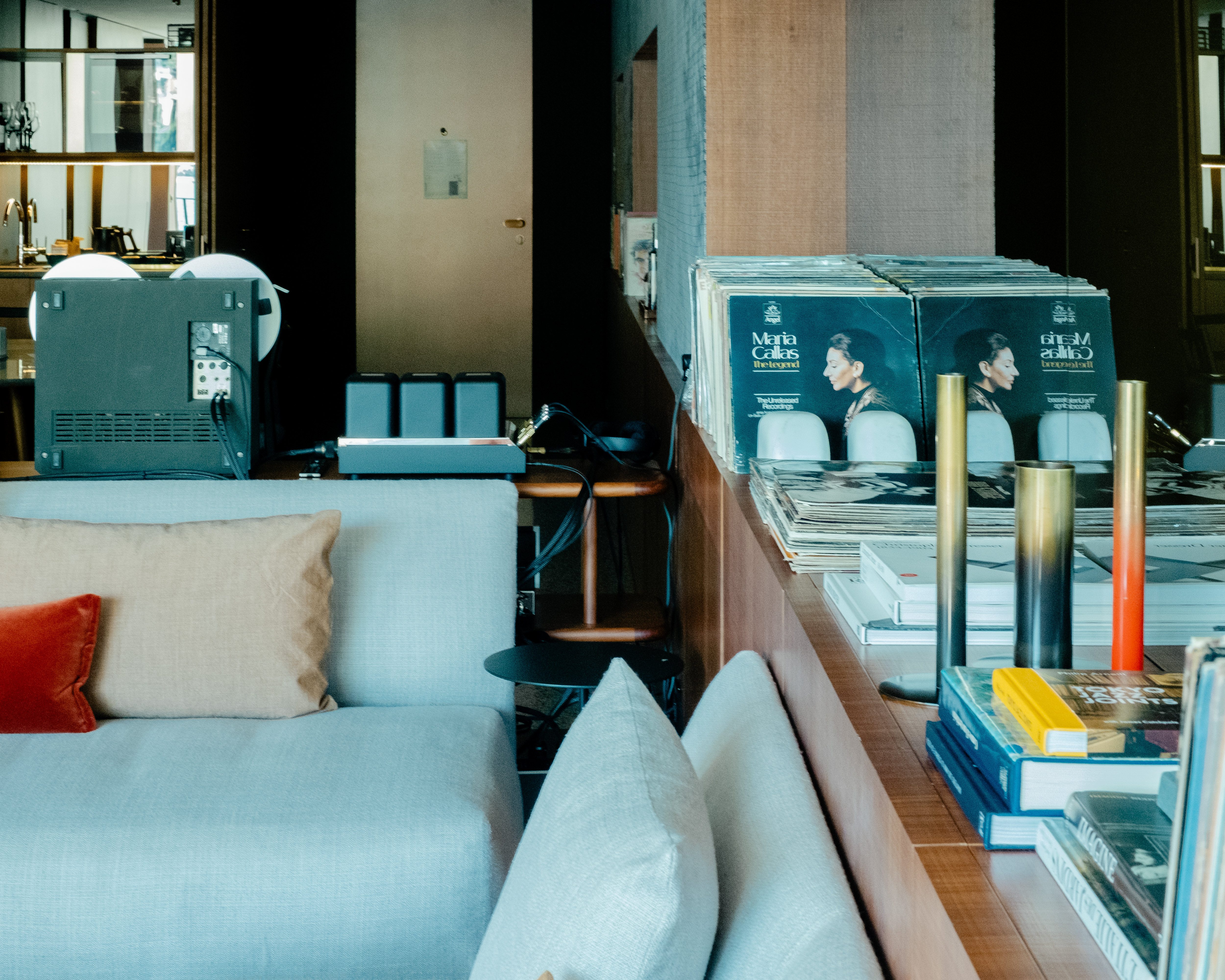 A high-fidelity listening suite fitted with retro-inspired music gear features floor-to-wall windows capturing the natural beauty of a lake and mid-century furniture with natural hues and textural furnishings.