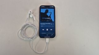 Apple EarPods USB-C plugged into iPhone 16 with Apple Music showing on the handset's display