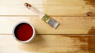 Tin of stain and paintbrush on bare wooden floor