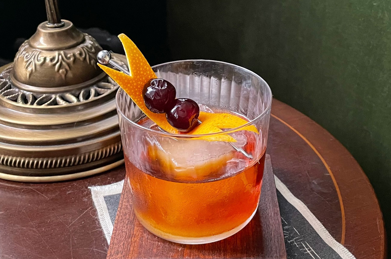 A cocktail in a tumbler on a wooden desk