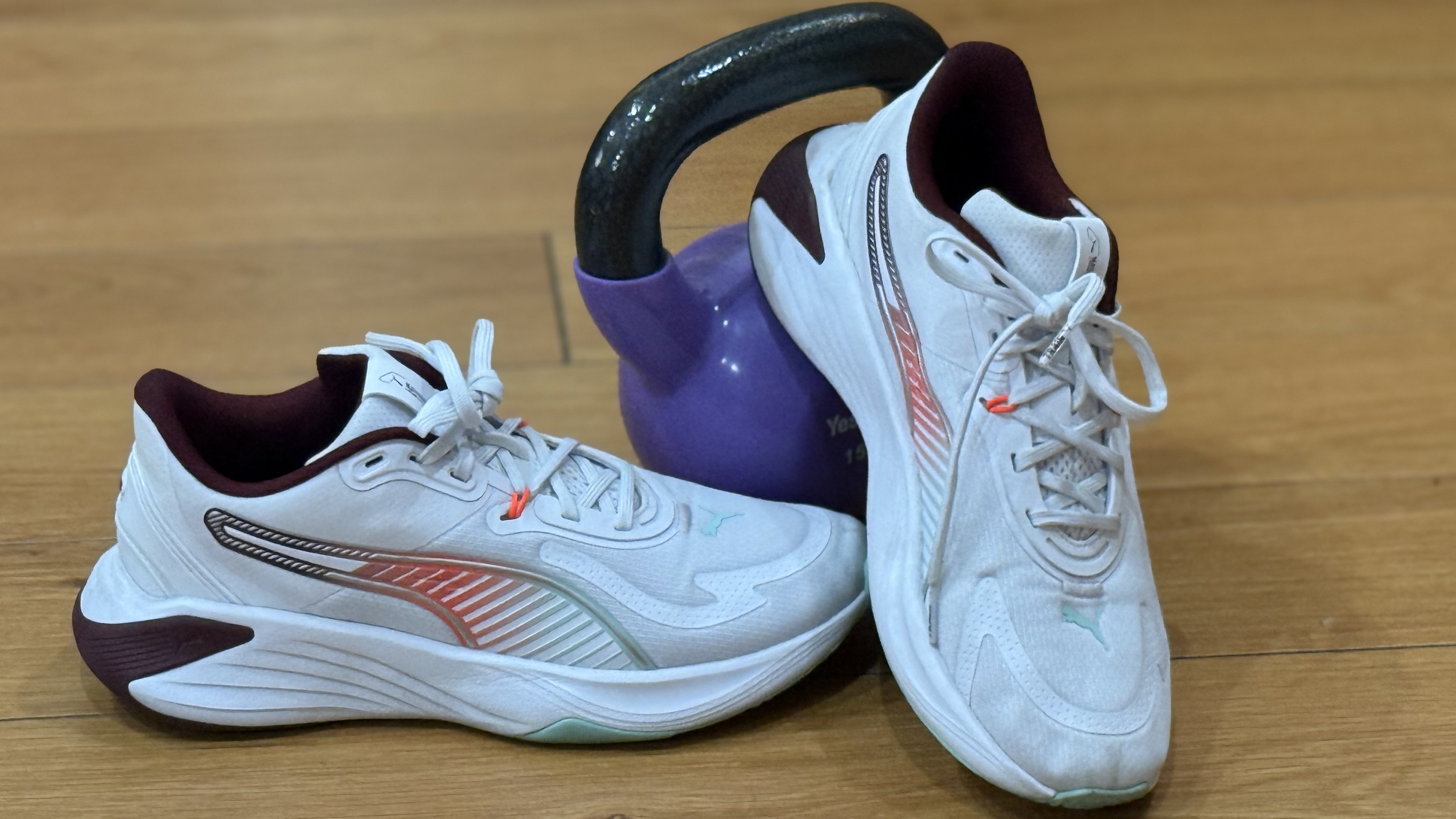 A pair of Puma PWR hybrid shoes on a wooden floor, with a kettlebell in the background.