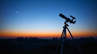 A photograph of a telescope in front of two bright objects in the night sky.