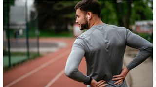 Sciatica: Man holding his lower back in pain during workout on a running track
