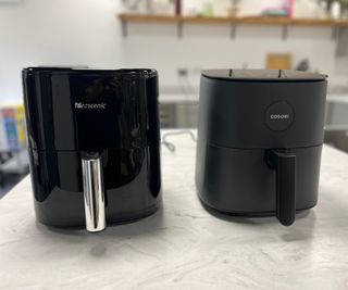 A Cosori Pro LE Air Fryer next to a Prosenic T22 air fryer on a kitchen counter.
